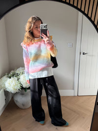 Person wearing a colorful sweater and black satin loose trousers taking a mirror selfie in a room with white walls and a vase of flowers. Paired with green adidas speziales to match the green in the rainbow style jumper.
