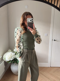 Khaki jumper with polka dot sheer sleeves paired with khaki tailored trousers.