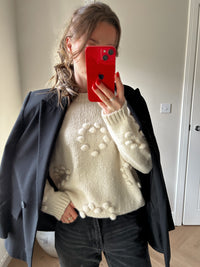 Woman wearing a cream jumper with pom-poms detailing.