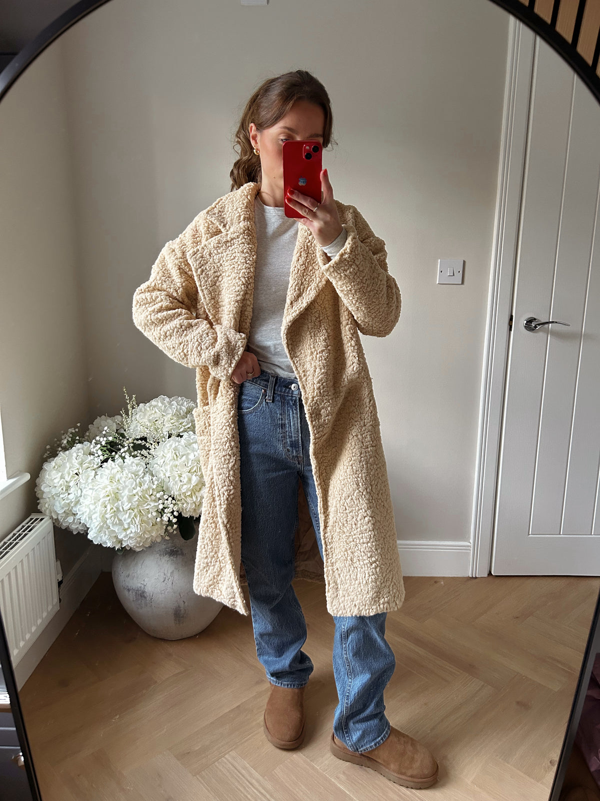 Person wearing a beige sherpa coat paired with blue jeans and a grey tshirt.
