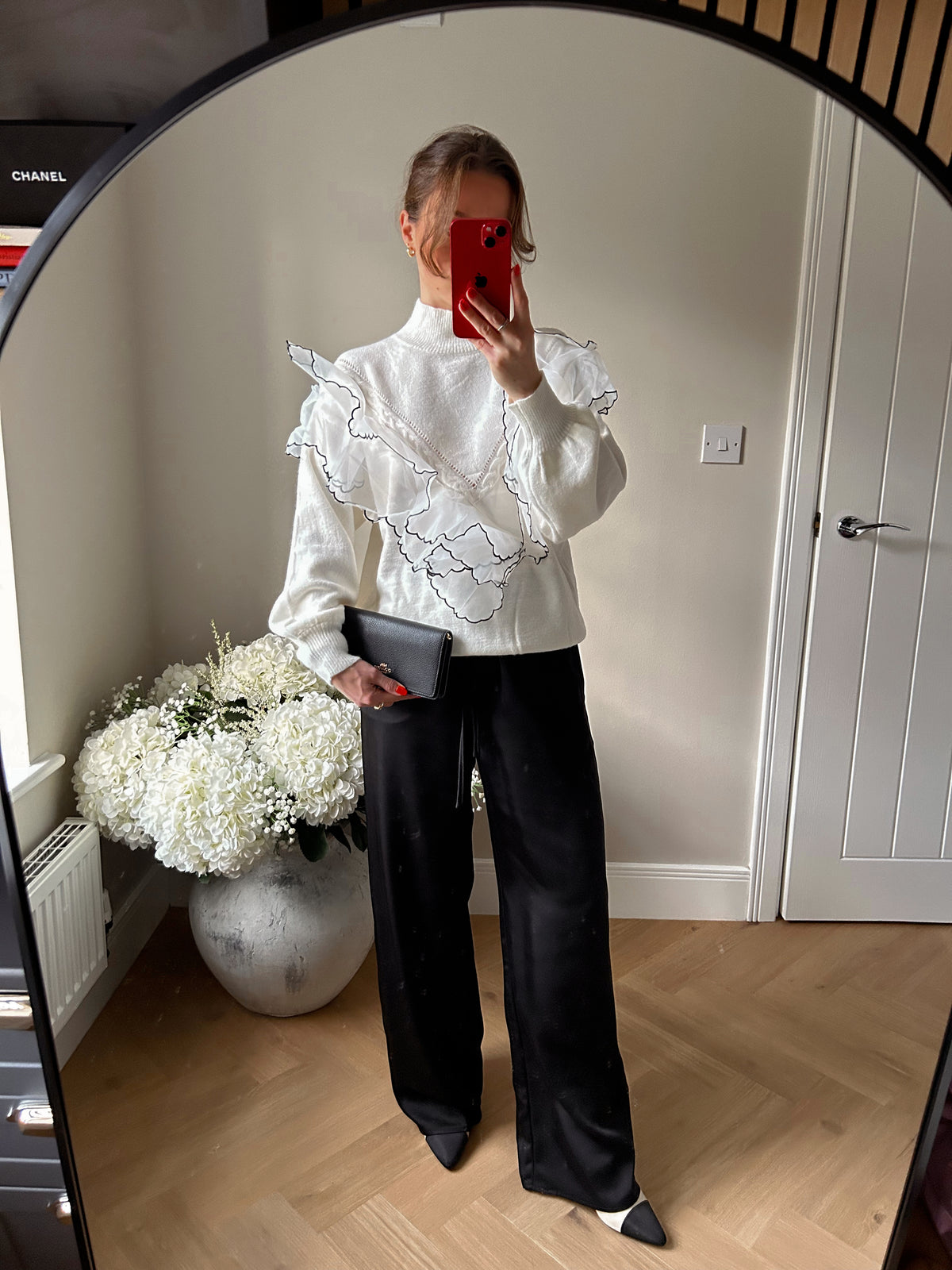 White high neck jumper with ruffle detailing in a v shape. Paired with black trousers and pointed heels.