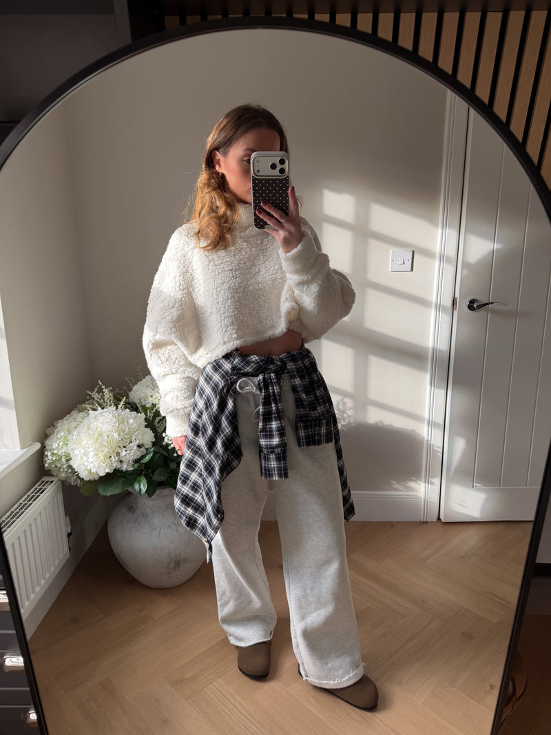 Cream soft fleecy cropped long sleeve jumper paired with grey joggers and shirt tied around the waist.