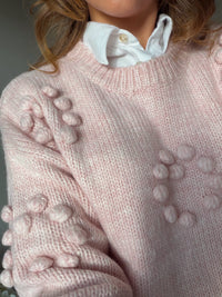close up of pink round neck jumper with pom poms.