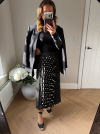 Woman wearing a black long sleeved top, oversized blazer over the shoulders and a white and black pleated polka dot skirt 