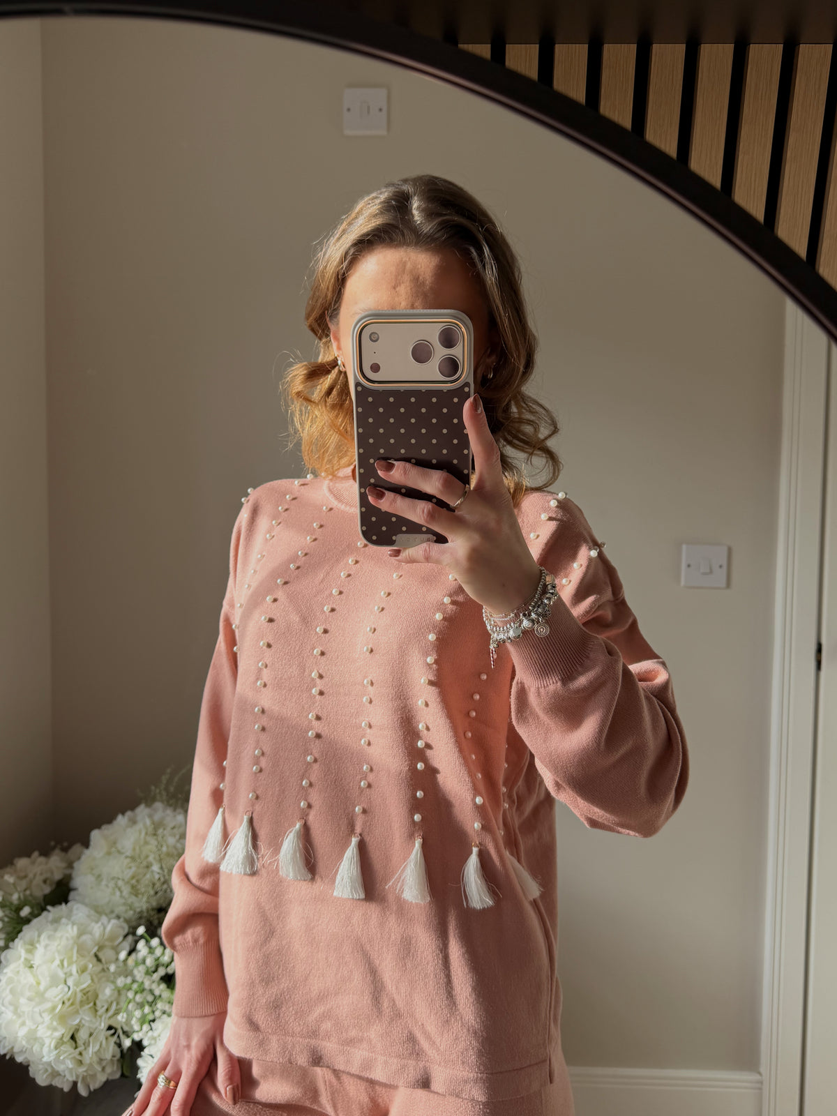 Person wearing a pink round neck jumper with pearl and tassel details.